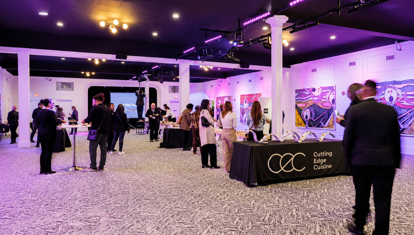 Event guests mingling near a "Cutting Edge Cuisine" table with colorful wall art